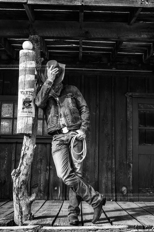 Hombre con estilo vaquero de la colección Bandido usando chamarra de mezclilla, sombrero y cuerda, apoyado en un poste con cartel de 'Wanted' en blanco y negro
